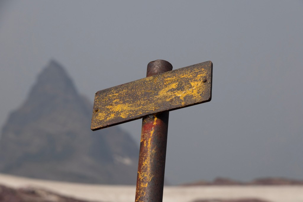 A metal sign post whose message has been weathered away fills the center of the frame.