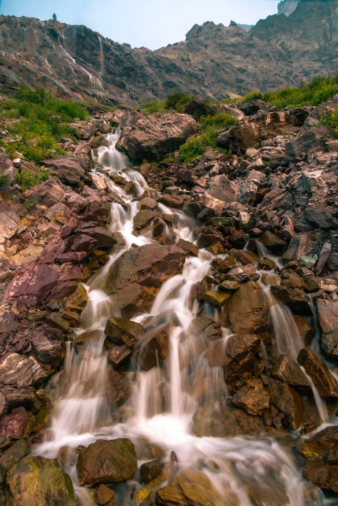 A waterfall cascades down a rocky slope, dividing into two waterfalls toward the bottom of the frame.