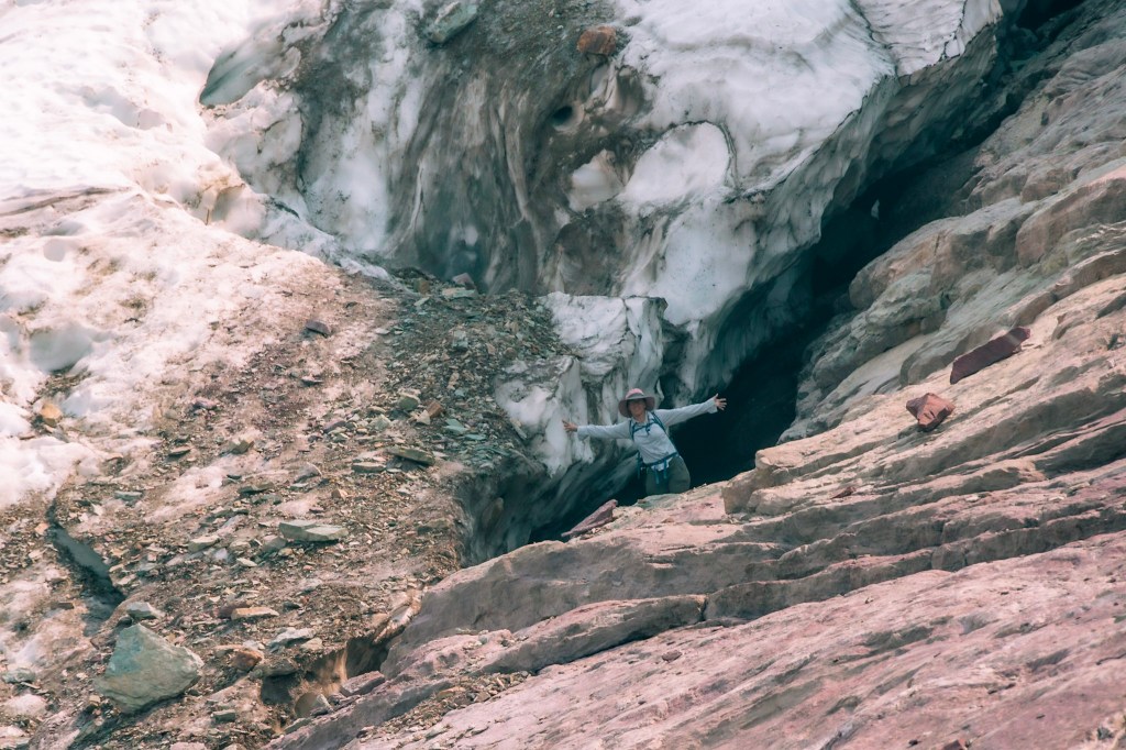 A closer shot of Laura standing between Sperry Glacier and the rock wall. She has her arms spread wide, right hand touching the glacier.