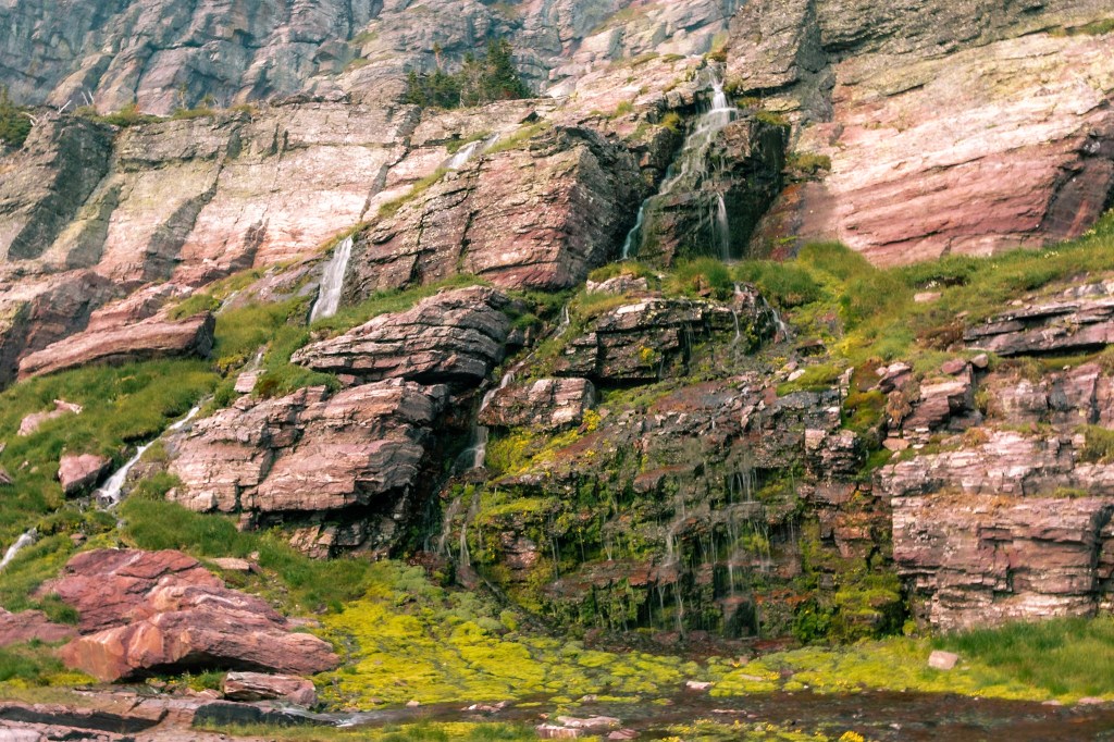 A waterfall descends yellow and red striped cliffs in the center of the photo. The cliffs have turned green where the water flows. 