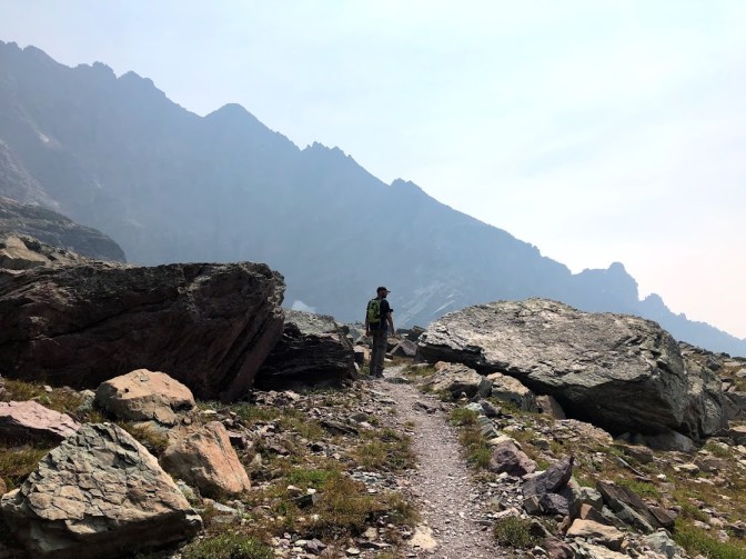 Dustin, in the distance at the center of the photo, with his back to the camera. Large rocks surround him with dark mountains in the background.