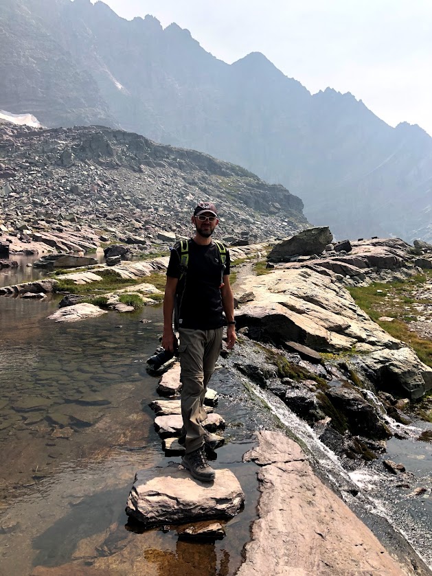Dustin, in the center of the photo, looks at the camera as he crosses the rocks across Feather Woman Lake, which falls off as a waterfall to the right.