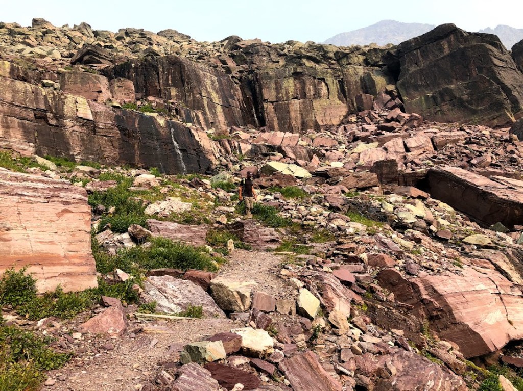 A rocky landscape with Dustin appearing very small in the center, walking toward the camera.