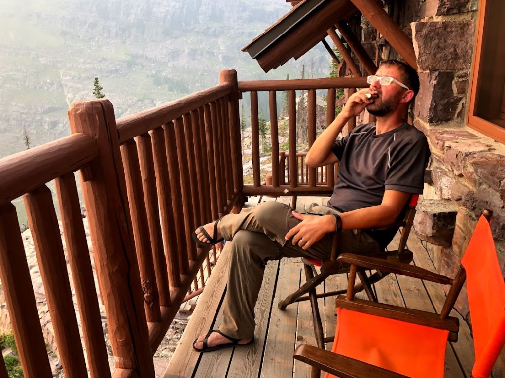 Dustin sits on a log balcony on the right side of the frame, tossing back a shot of victory scotch. 