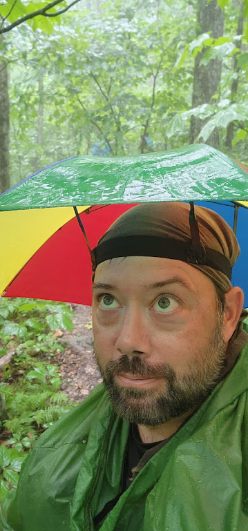 A portrait of Hobz wearing his umbrella hat, eyes turned upward to watch the rain hit the umbrella.