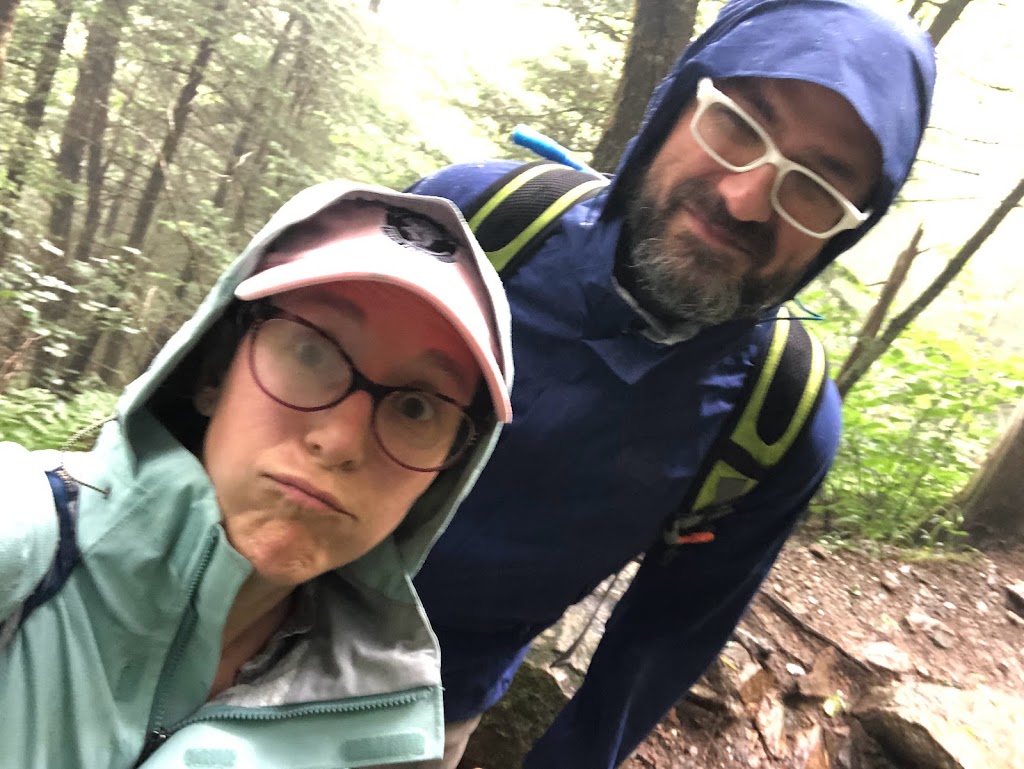 Selfie of Laura nd Dustin. Laura looks a little put out, Dustin is smiling. Both wear rain jackets that are slightly damp.