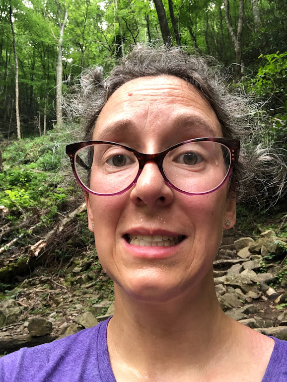 A selfie of Laura, whose face fills the whole frame. Her face is red with beads of sweat running down it. Whisps of her otherwise-pulled-back hair stick out in every direction. She wears a pained smile.