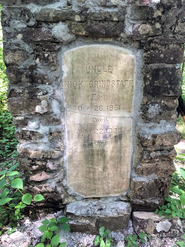 A stone monument fills the whole frame. It is mostly constructed of found stones mortared together, but in the center is a carved tomb stone reading: 

UNCLE 
NICK GRINDSTAFF
Born
Dec. 26, 1851
Died
July 22, 1923

[obscured text below]