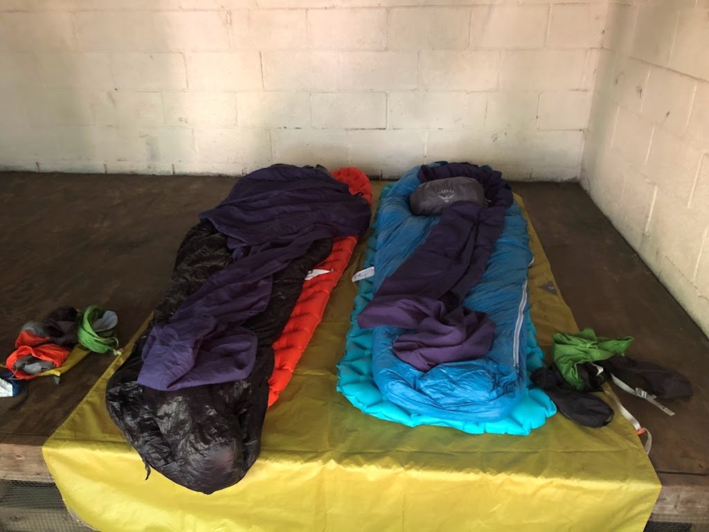 Close up shot of two sleeping bags laid out on the shelter platform, on top of a tent footprint being used like a tarp.
