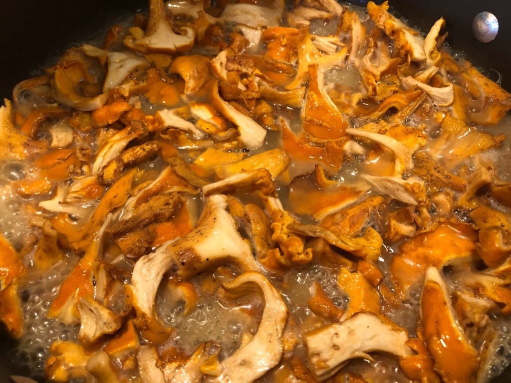 Close up of many sliced orange mushrooms cooking in a pan.