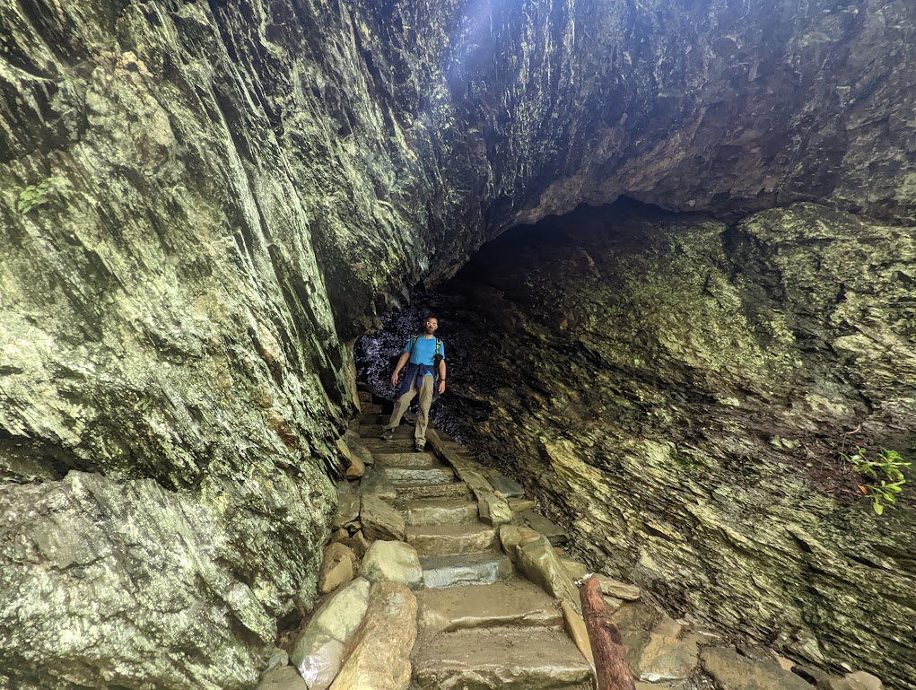 Dustin, small in the center of the frame, stands on a stone stairway that is surrounded on all sides - including the top - by yellow-gray stone. The staircase runs through a small opening in the stone, which is where Dustin is standing.