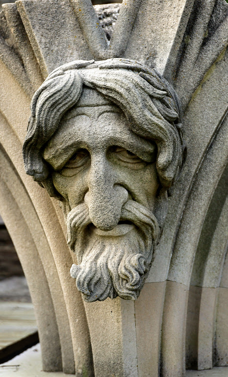 A cathedral grotesque featuring the face of a bearded man with an immense nose and very droopy eyebrows. 