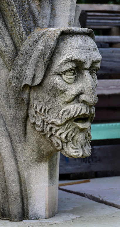 A cathedral grotesque featuring the face of a bearded man wearing a cloth on his head. 