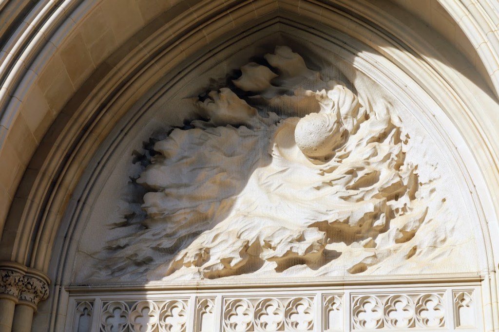 A deep bas-relief sculpture depicting the creation of the moon. The moon is center-right with billowing clouds of creation swirling around it.