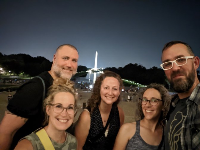 Tour group members pose for an out-of-focus group selfie with the Washinton Memorial and reflecting pool in the background.