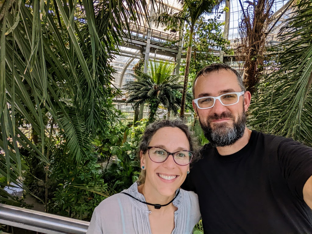 Laura and Dustin pose for an off-center photo inside the National Botanical Gardens, with tropical plants in the background.