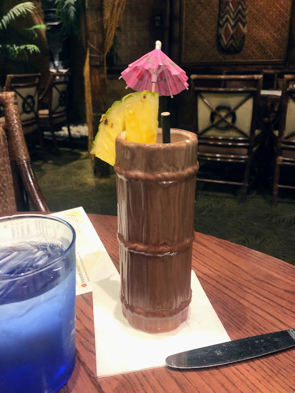 A tall, tiki-style mug fills the frame with a wedge of pineapple and pink paper umbrella. 