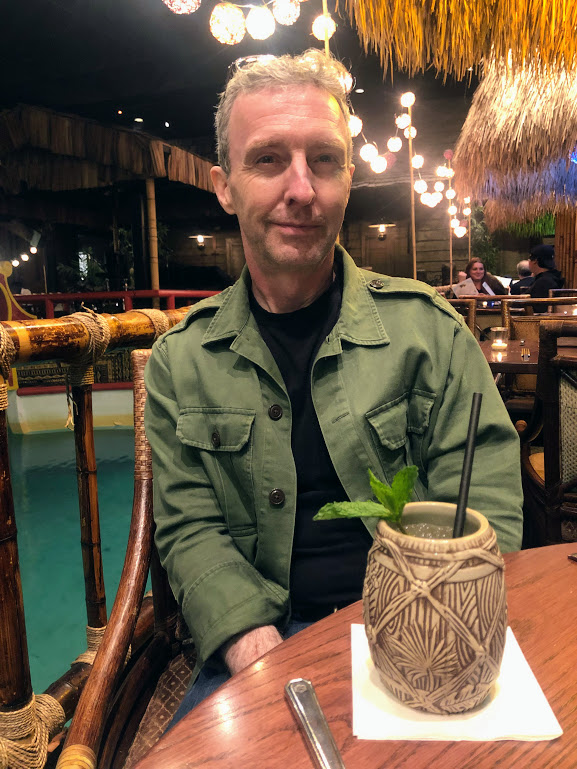 Matt sits behind a drink shaped like a tiki barrel (if that's a thing). A sprig of mint sticks out of the cup.