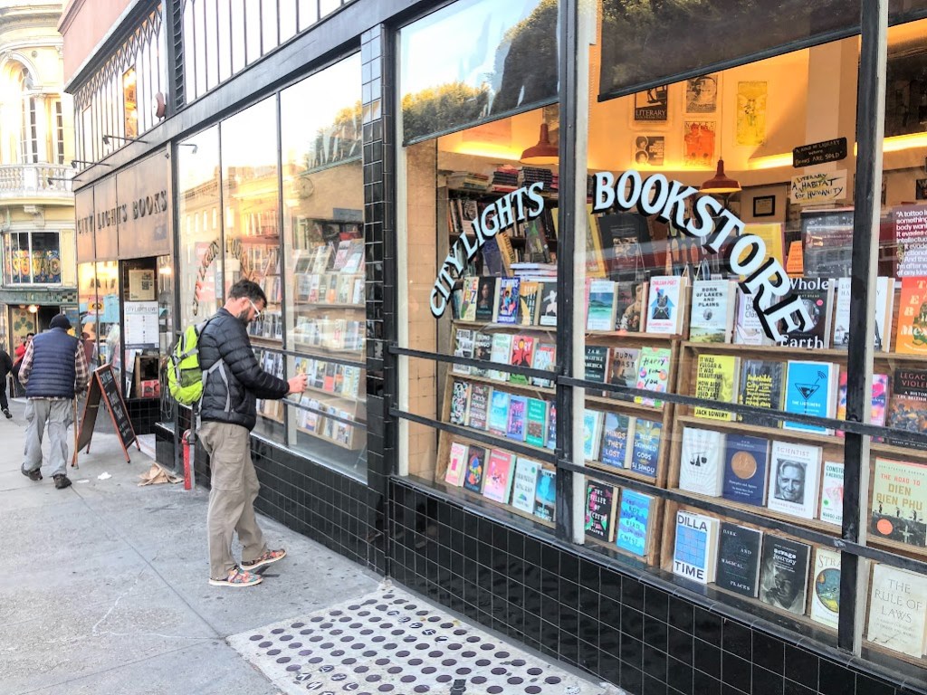Dustin stands in front of the City Lights Bookstore, looking in through the very large windows at the displays of books inside.