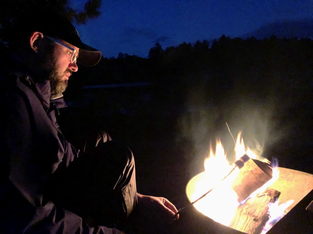 Dustin, left, holds a stick with two marshmallows over a fire to his right. He watches the marshmallows intently. This is serious business. 