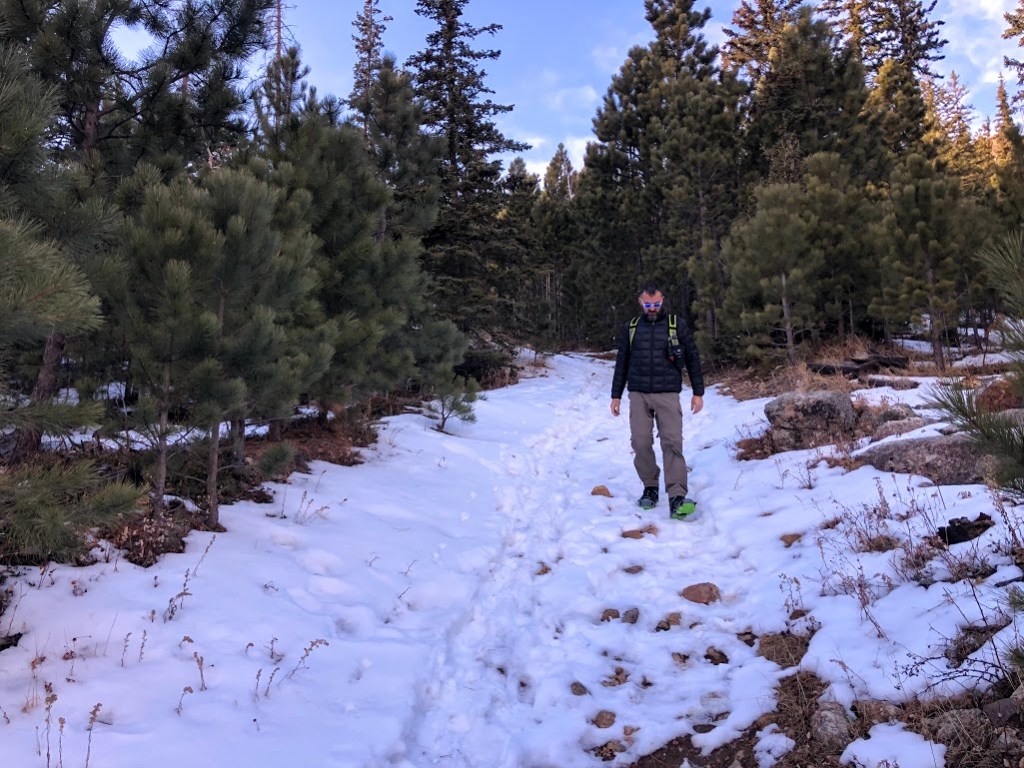 Dustin picks his way down a slope toward the camera. The slope has well-worn foot tracks, and is covered with snow and rocks.