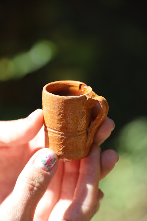 Closeup of a very tiny red clay mug (two inches tall?) held by fingers with flamingos painted on the nails.