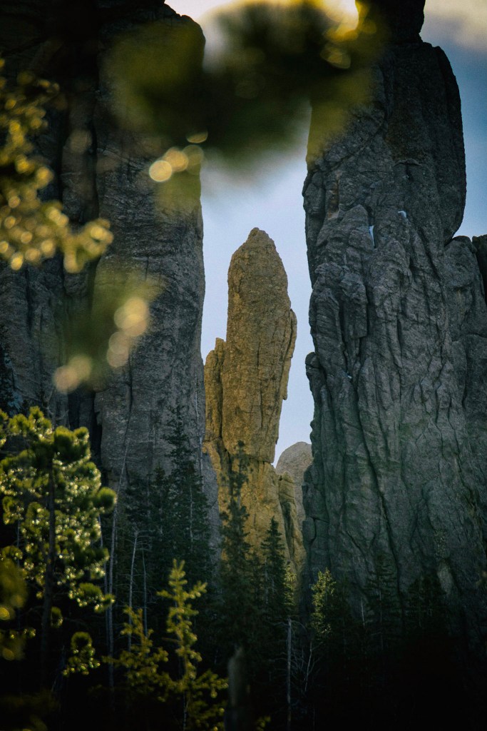 A photo of a granite spire taken from between two other granite spires. The most distant spire is in focus, with the two framing it fuzzy.