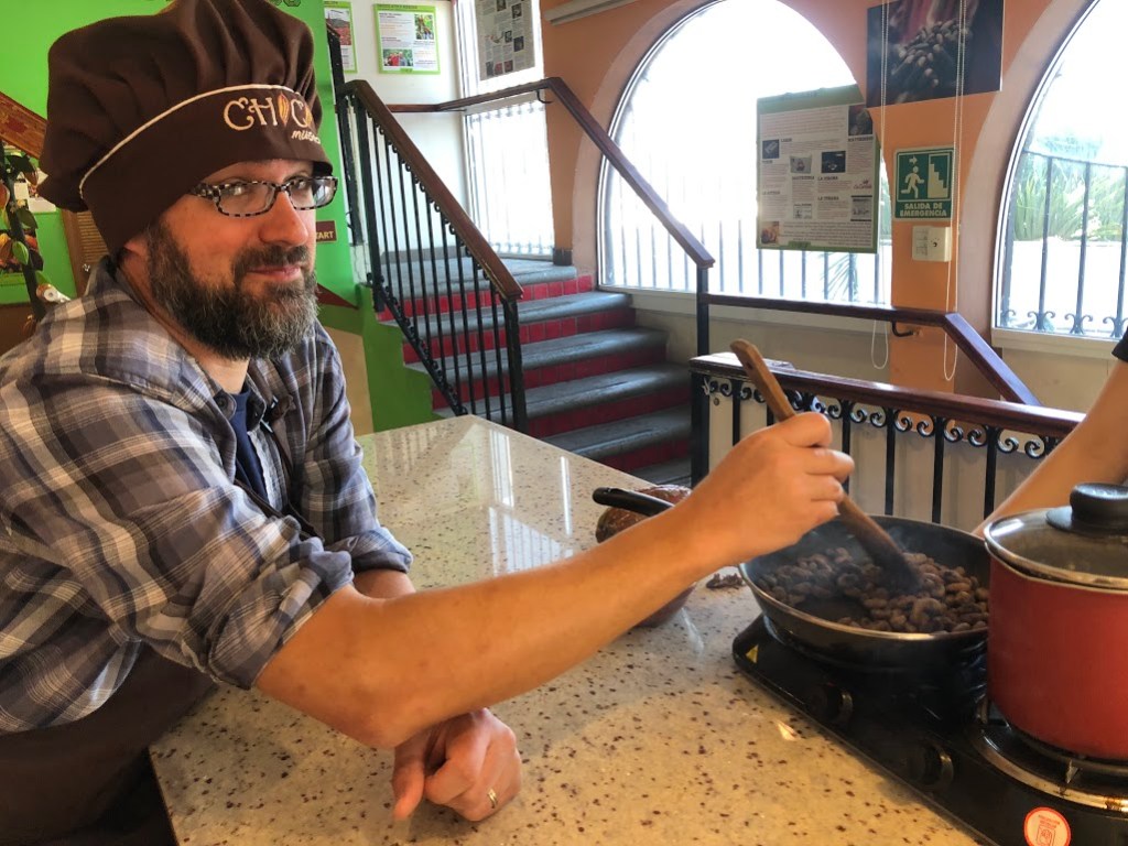 Dustin smirks at the camera while stirring the roasting cacao beans.