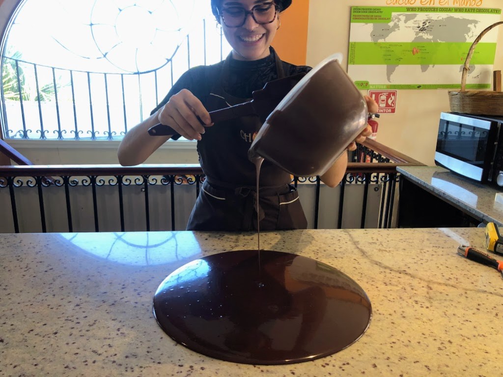 Lizzette, smiling, pours the chocolate from the big bowl onto the granite countertop. It has formed a large, shiny, perfect circle of chocolate in front of her.