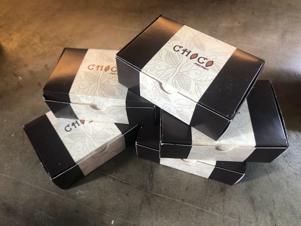 A closeup of five white and black cardboard boxes labeled "ChocoMuseo" stacked up on a counter."